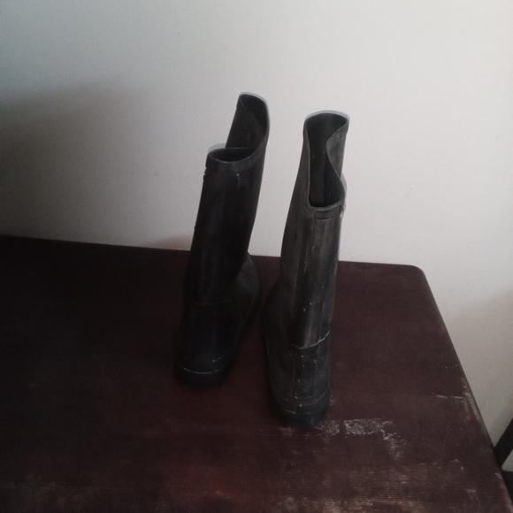 A close-up photo of a pair of black rubber boots with a worn tread sitting on a - Picture 1 of 3